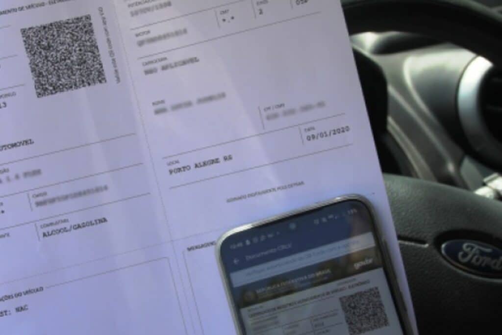 Documento veicular e celular sobre volante de carro.