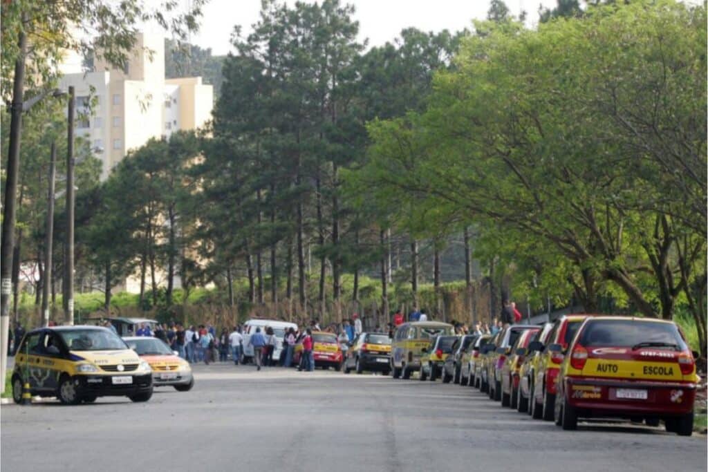 Autoescolas estacionadas em rua arborizada.