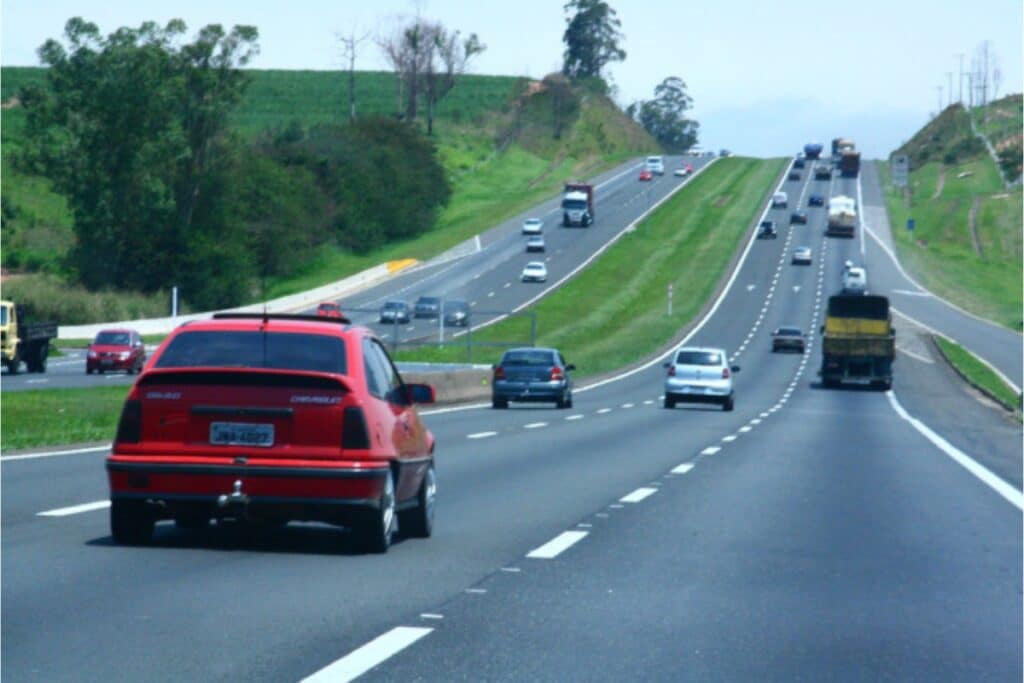 Trânsito em rodovia com veículos e paisagem verde.