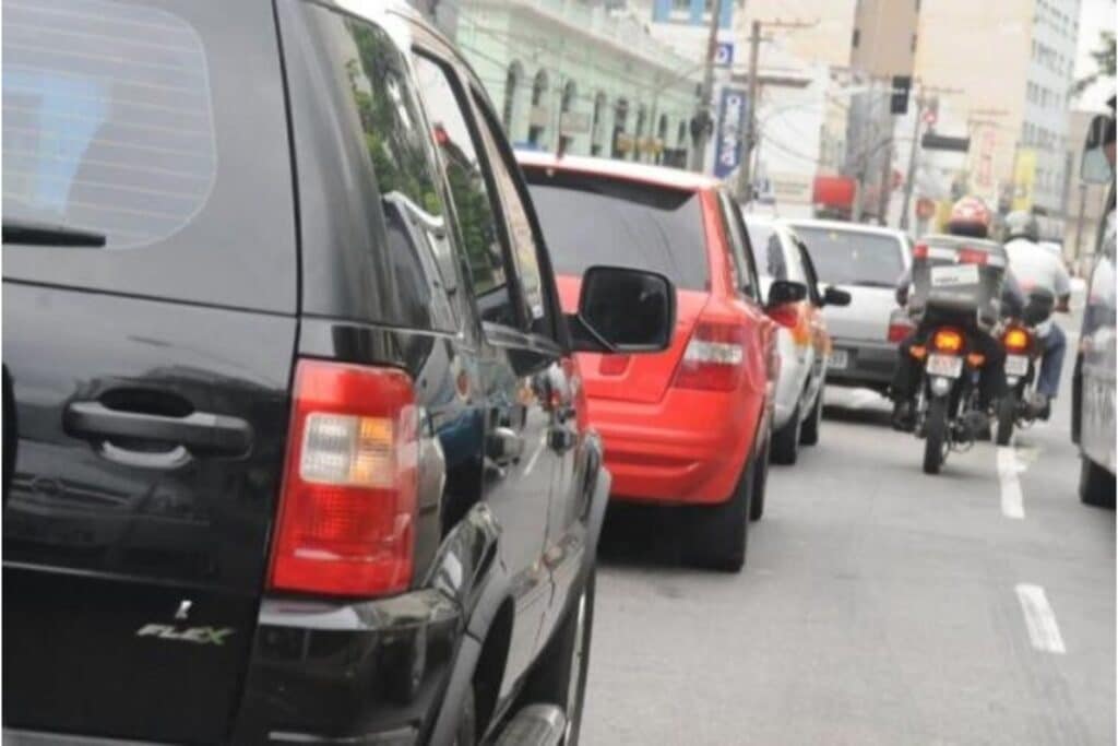 Trânsito congestionado com carros e motos em avenida.